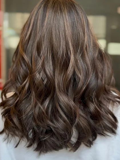 A beautiful example of a chocolate California brunette style. The subtle, warm highlights woven through the dark base create a natural, sun-kissed look, and the soft waves enhance the dimension.