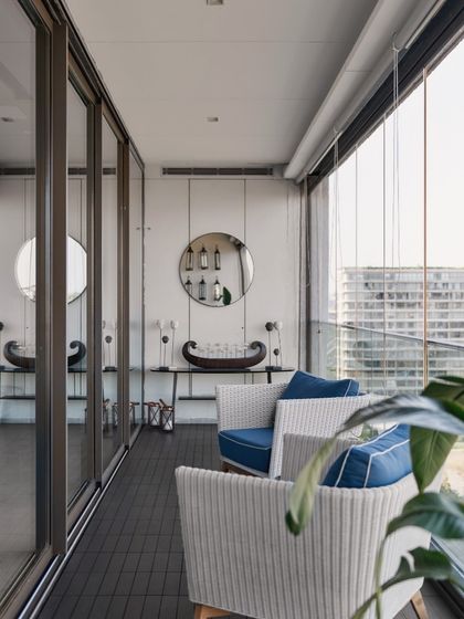 We elevated this balcony by blending elegance and comfort. Chic wicker armchairs with plush blue cushions are paired with a sleek console table and a circular mirror, creating a serene outdoor area for unwinding with a view of the city.