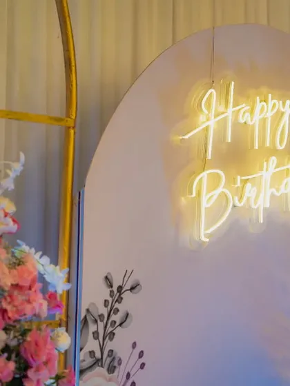 Another angle of the "Happy Birthday" neon sign, highlighting its warm glow against the soft pink backdrop and lush floral arrangements.