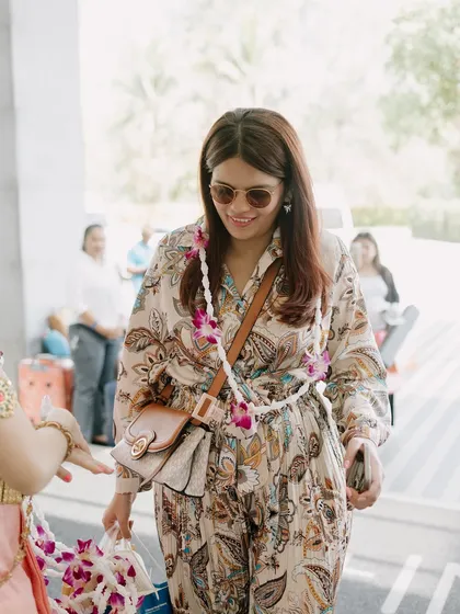 A smiling guest, adorned with a fresh orchid garland, arriving at a destination wedding in Thailand.