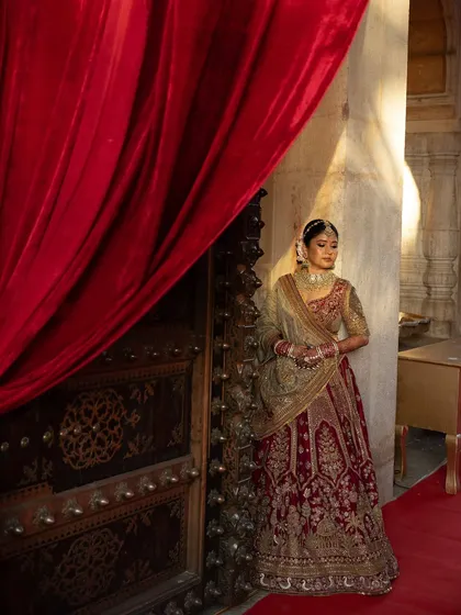 The bride, a vision in her red and gold lehenga, poses against the rich, historic textures of the Chomu Palace. We work with you to ensure your bridal portraits capture the essence of your chosen venue.