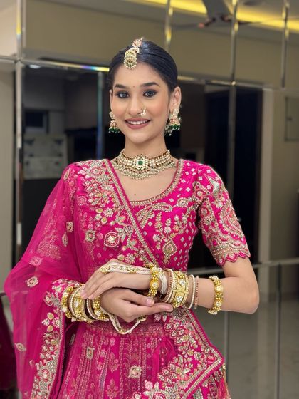 A vibrant and happy bride in a stunning pink lehenga. This look, with its fresh flower bun and dewy makeup, is perfect for a daytime wedding or Mehendi ceremony.