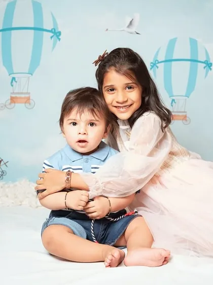 Capturing the sweet, natural bond between siblings. This portrait shows a big sister's loving hug during a fun studio session with a hot air balloon backdrop.
