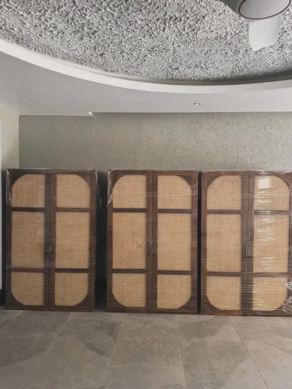 Three finished wardrobes with large, curved cane panels, wrapped and ready for delivery to a client's home.
