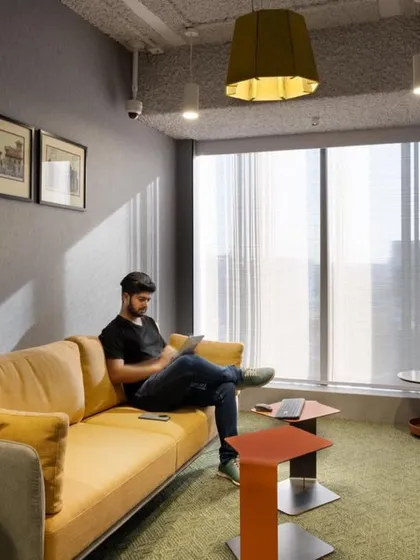 A comfortable yellow sofa provides a spot for an employee to relax and work informally. The large window allows for plenty of natural light.
