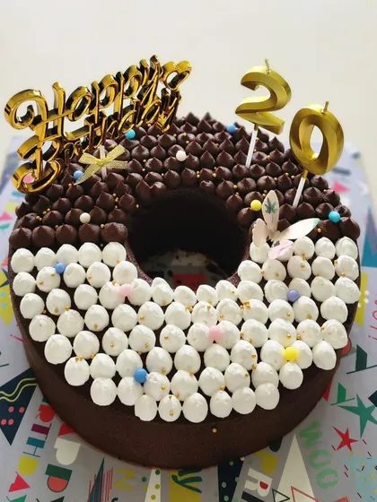 For a fun 20th birthday, I created this donut-shaped cake. It's half chocolate with ganache piping and half vanilla with marshmallow-style buttercream dots, combining two delicious flavours in one unique design.
