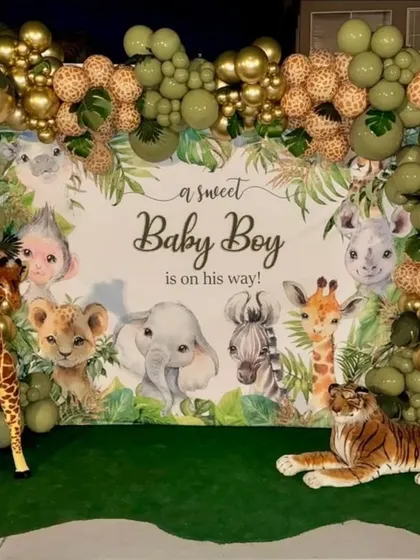 A jungle-themed baby shower backdrop announcing "a sweet Baby Boy is on his way," framed by a lush balloon garland and accompanied by plush animal props.