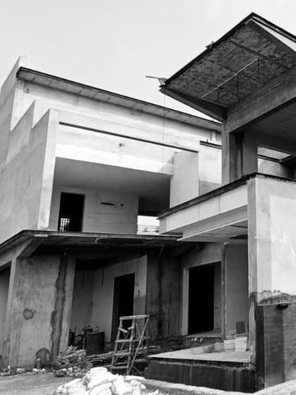 The exterior of a house during the structural phase, with open walls and exposed concrete slabs showing the building's geometric massing.