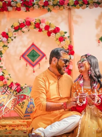 A portrait of the happy couple seated at their Haldi ceremony, surrounded by colorful decor elements like embroidered umbrellas. This is a perfect summary of their special day.