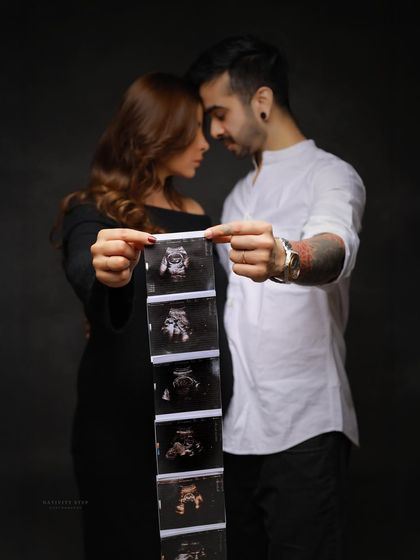 A creative couple's portrait where they hold a strip of ultrasound photos. The dark, moody lighting adds a touch of drama and intimacy.