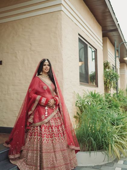 Kanika's full look against the lush greenery. The red of her outfit pops, while her makeup remains elegant and understated.