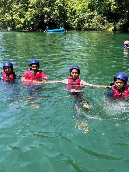 Four girls hold hands and float in the clear green water of the Kali River, enjoying a swim break during their camp.