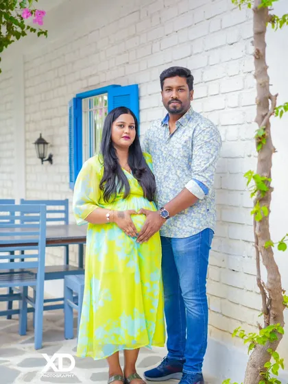 A classic couple's pose with hands forming a heart on the belly, set against a bright and cheerful backdrop.