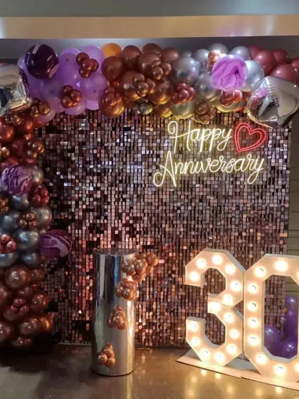 A glamorous 30th-anniversary party with a rose gold shimmer wall, a balloon arch, and large '30' marquee numbers.