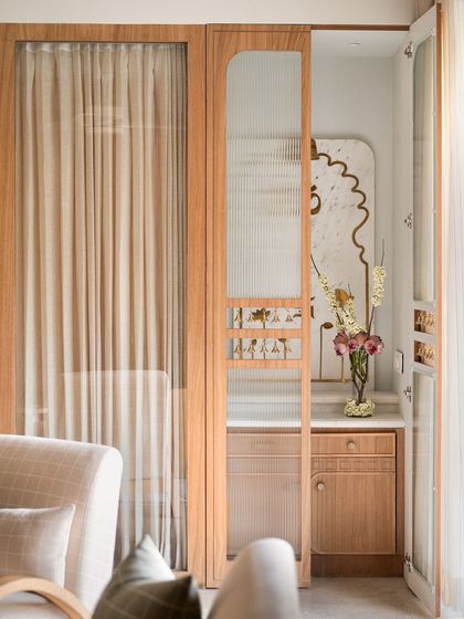 For the mandir in the Kābu home, we created a space that is minimal yet warm and elegant. We designed a marble back panel with brass inlaid lotuses and religious motifs, enclosed by a fluted glass door to add to the pious charm.