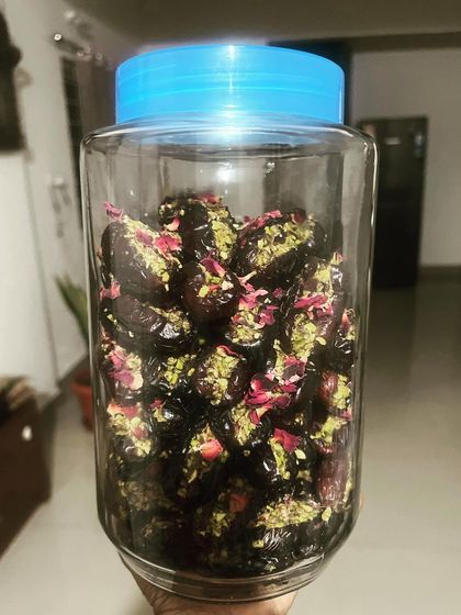 A large jar filled with my gourmet stuffed dates. Each date is generously filled with pistachios and garnished with rose petals, ready for a large order or a festive celebration.