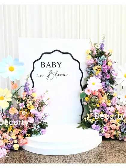 A 'Baby in Bloom' backdrop with a different design, featuring a wavy border and colorful floral arrangements with large daisy props.