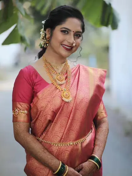 A smiling portrait of a bride ready for her South Indian engagement ceremony, looking radiant in a pink silk saree and gold jewelry.