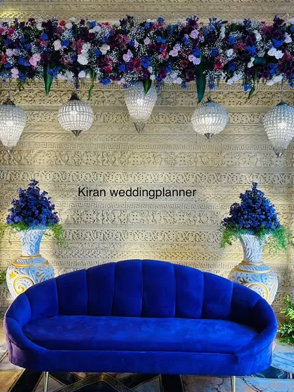 A royal blue and purple themed stage setup. The deep blue sofa is complemented by ornate vases, crystal chandeliers, and a textured backdrop, creating a look of pure luxury.