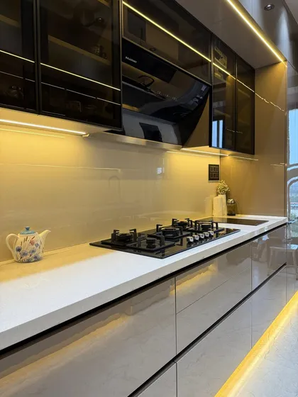This parallel kitchen design maximizes efficiency in a compact space. This view shows the clean lines of the quartz countertop, the integrated hob, and the reflective high-gloss laminate finish on the lower cabinets.