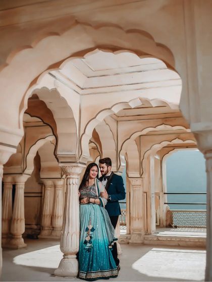 A full-length portrait of the couple standing among the beautiful scalloped arches of a palace corridor, showcasing their elegant outfits.