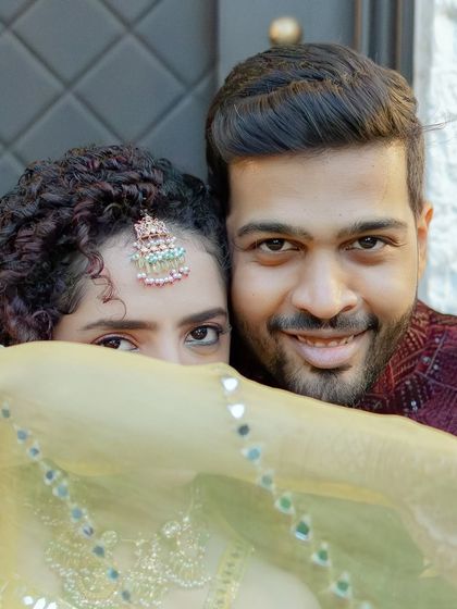 A playful and intimate portrait from a cocktail event. The bride peeks from behind her dupatta, sharing a secret smile with her partner in this fun and candid shot.