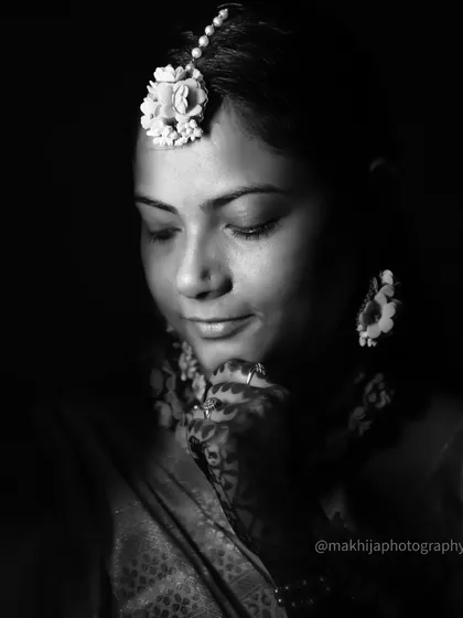 A close-up black and white portrait of the bride. This intimate shot captures her serene expression and the intricate details of her floral maang tikka.