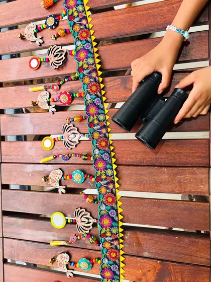 My daughter's hands with binoculars, playfully inspecting the 'Tamaara' toran. It’s a piece of art that brings joy to the whole family.
