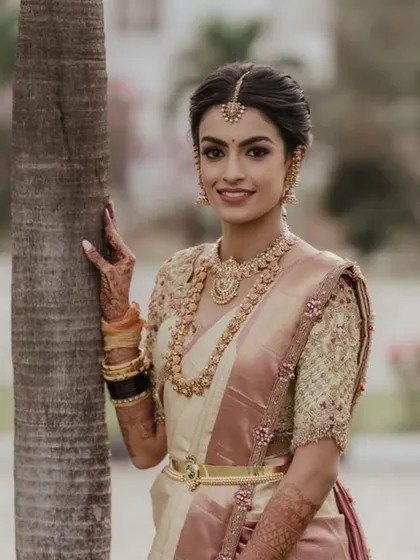 A smiling bride in her custom off white and pink Kanjivaram saree. The heavily embroidered blouse and traditional gold jewelry create a classic and timeless South Indian bridal look.