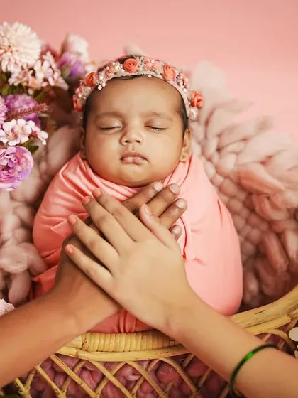 The parents' hands gently cradle their newborn daughter in her basket, symbolizing their protection and love. This detail shot is a meaningful addition to any newborn gallery.