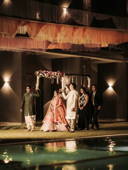 The bride's grand entrance for the poolside ring ceremony. Escorted by her family under a floral canopy, this wide shot captures the beautiful ambiance and anticipation of the moment.
