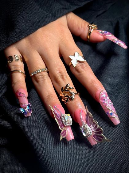 This view shows the full set of long, elegant nails, adorned with multiple rings to complete the look.