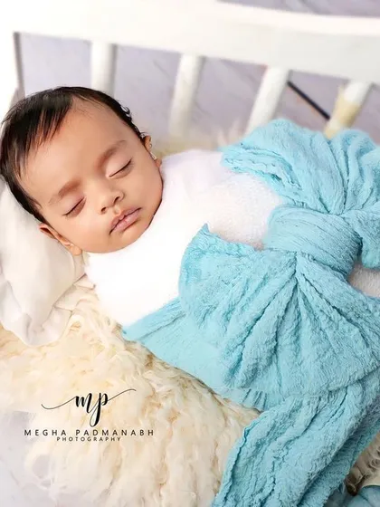 A baby boy sleeping on a white bench, wrapped in a blue bow. The blue-toned pumpkins add a charming, rustic feel.
