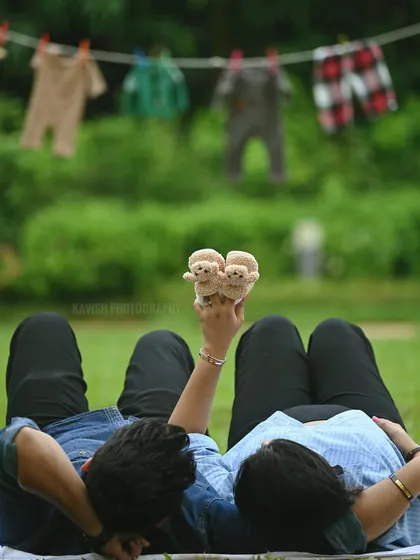 A creative and symbolic maternity shot, with the couple lying on the grass holding up a pair of tiny baby shoes.