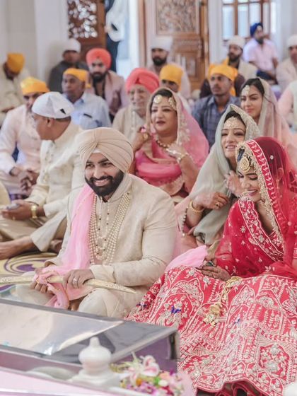 A candid moment of the bride and groom smiling during their Anand Karaj ceremony, surrounded by their families. This image captures the communal joy of the occasion.
