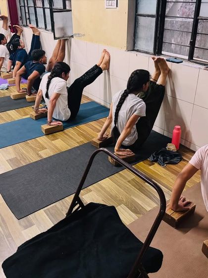 Students use the wall and yoga blocks to work on their leg strength and flexibility. This supported L-sit pose is excellent for building core and arm strength.