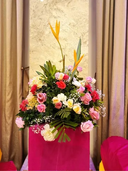 A beautiful floral arrangement in a bright pink vase, using a mix of roses and birds of paradise to match the colorful Haldi theme.