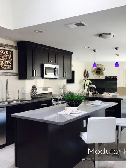 A classic dark-themed modular kitchen with an island counter. This design provides ample storage and workspace, seamlessly integrating with the open-plan living area.
