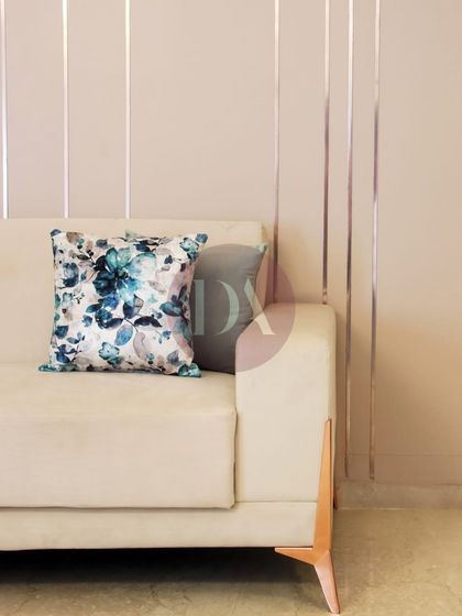 A detail shot of a beige sofa with a beautiful blue floral cushion. The subtle silver stripes on the wall behind add another layer of texture, showcasing our focus on crafting spaces with intention.