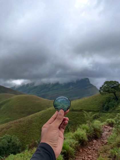Holding up our Kudremukha badge against the dramatic cloudy sky and green hills. A perfect memento of the trek.