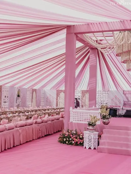 A magnificent reception setup under a flowing pink and white shamiyana tent. The entire space is bathed in our signature 'Gulabi Love' theme, creating a royal, fairytale ambiance for a truly memorable event.