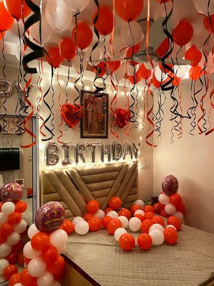 This energetic birthday setup features a mix of orange and white balloons, with black and red streamers hanging from the ceiling for a festive party atmosphere.