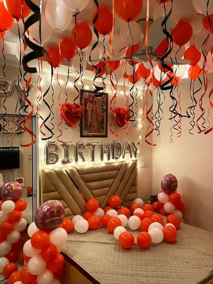 An orange and white themed birthday room setup with foil letters and balloons with ribbons covering the ceiling.