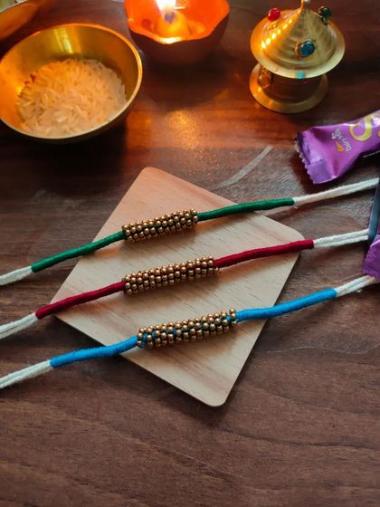 A set of simple and elegant rakhis made with thread and golden beads. These are available in green, red, and blue.