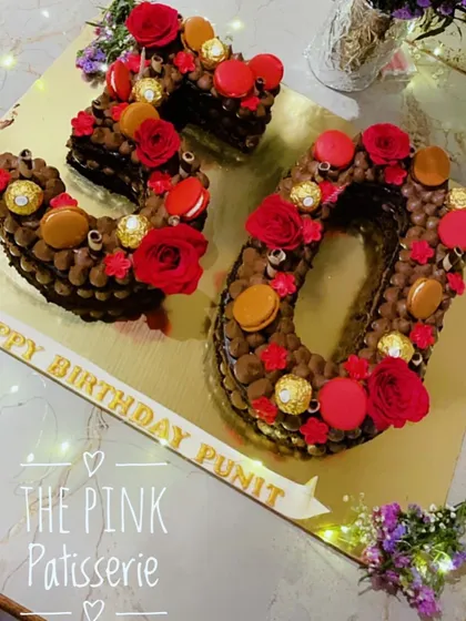 A rich, chocolatey monogram cake for a 30th birthday. This "30" shaped cake is decorated with chocolate buttercream, Ferrero Rocher, red roses, and macarons.
