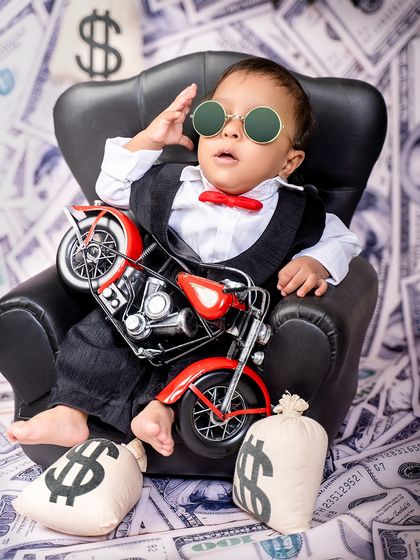 The boss baby takes a break. This little one relaxes in his chair with a toy motorcycle, looking cool and collected in his suit and bow tie.
