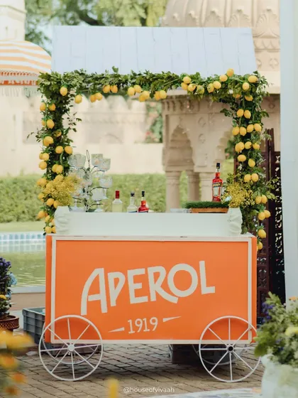 A bright orange Aperol cart, adorned with a garland of fresh lemons, perfectly capturing the Italian summer vibe of the Positano-themed event.