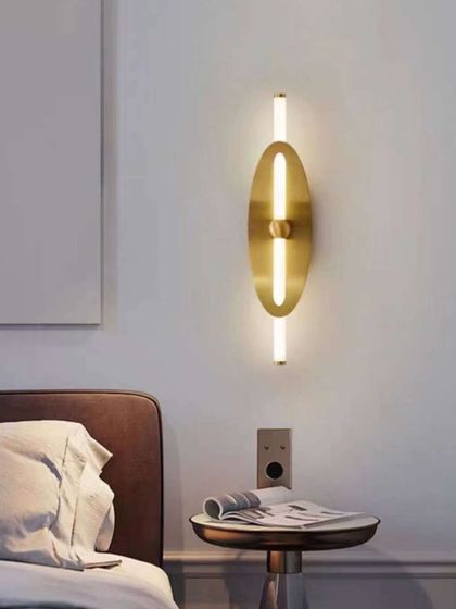 A sleek, minimalist wall sconce with a vertical light tube and an oval brass backplate. This fixture is perfect for adding a touch of modern elegance to a bedroom or hallway.