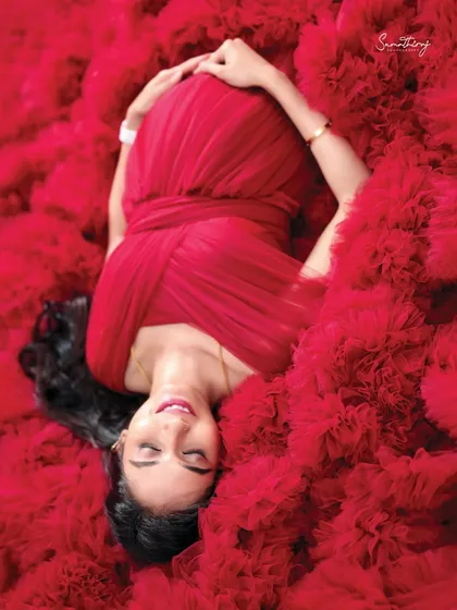A serene top-down shot of a mother-to-be in a red ruffled gown. Her peaceful expression and the sea of red fabric create a powerful and artistic image.