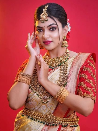 A full view of a bride adorned in our temple jewellery against a vibrant red background. This set includes a maang tikka, choker, haram, and Vaddanam for a complete and cohesive look.